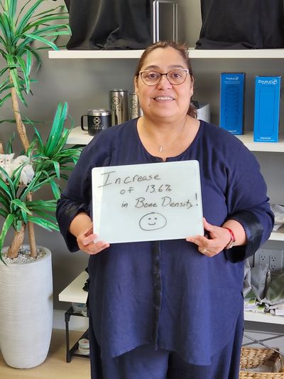 OsteoStrong member Minerva M. holding her whiteboard with DEXA numbers