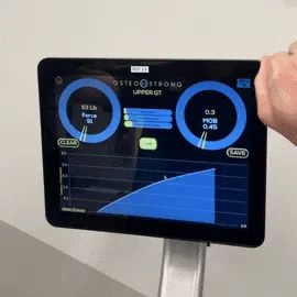 Woman using the OsteoStrong bone-loading device with a certified coach nearby