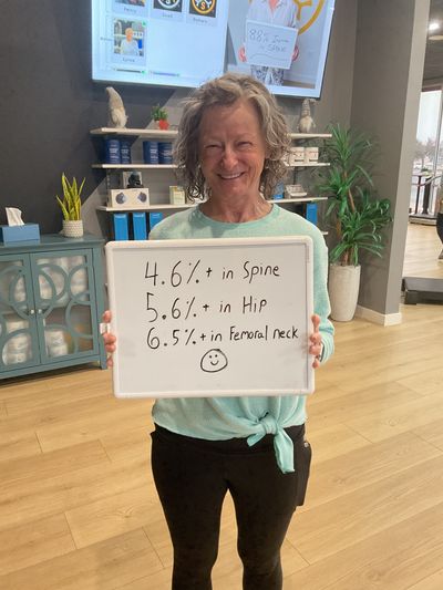 OsteoStrong member Pam R. holding her whiteboard with DEXA numbers