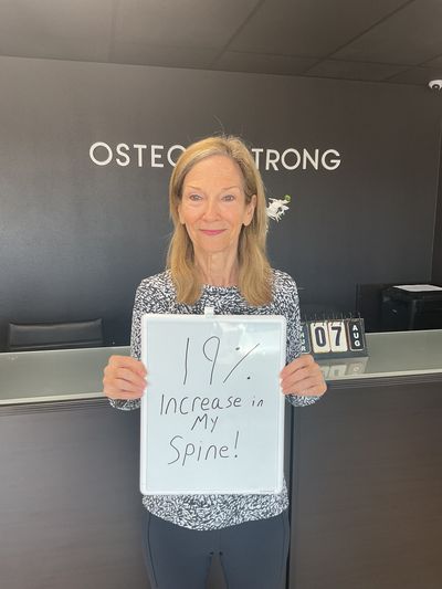 OsteoStrong member DeeDee holding her whiteboard with DEXA numbers